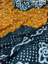 A bandhani style saree with black and yellow patterns on a fabric surface.