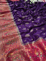 A purple and red Dola silk Banarasi saree with cutdana work, captured with a floral design at the border.