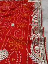 A saree with bandhani style patterns in orange and red colors, featuring detailed gotapatti work.