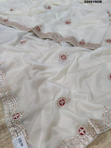 A cream-colored tissue silk saree with Bollywood-style embellishments and gotapatti work, including floral patterns and traditional border designs.