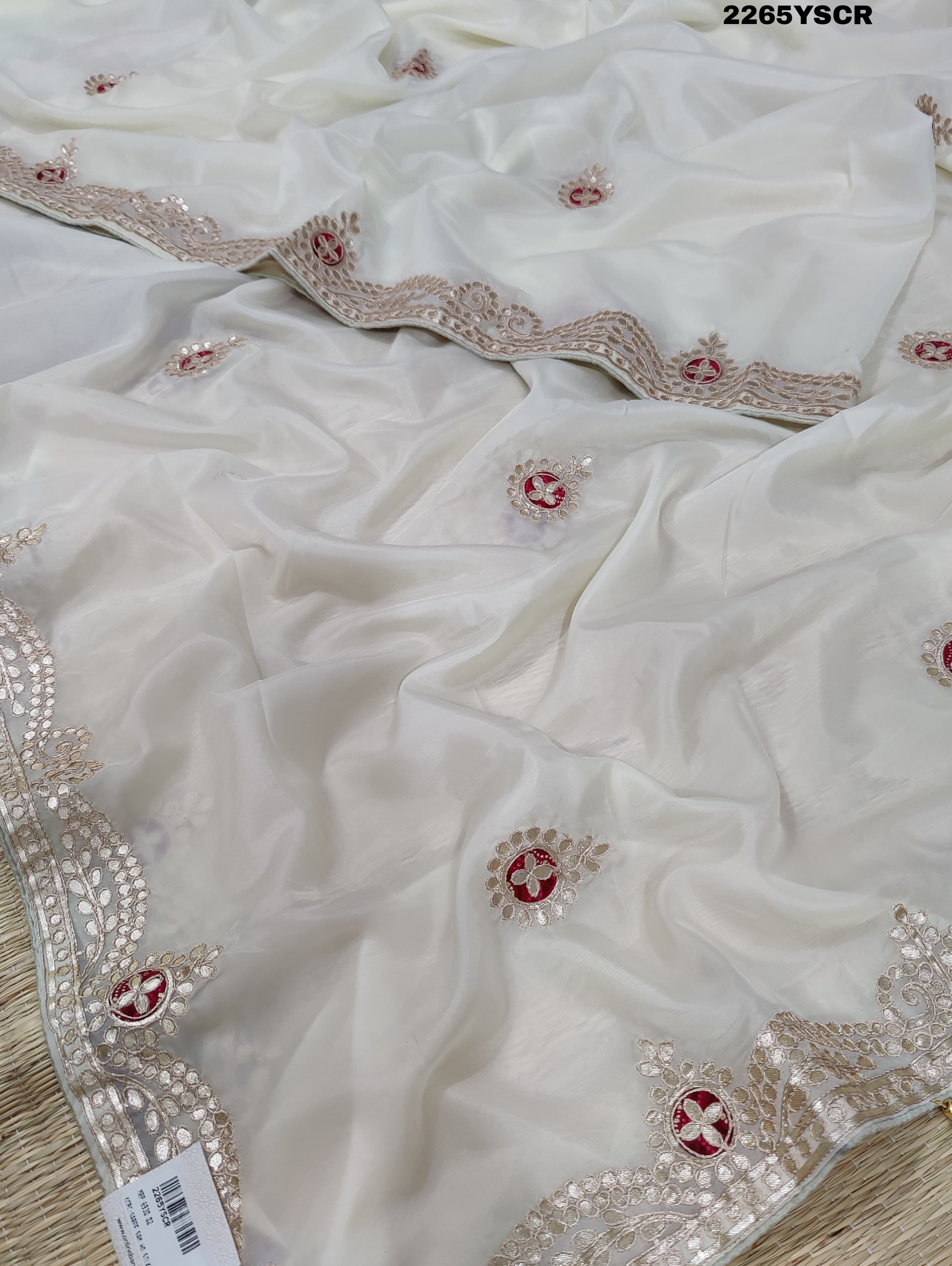 A cream-colored tissue silk saree with Bollywood-style embellishments and gotapatti work, including floral patterns and traditional border designs.