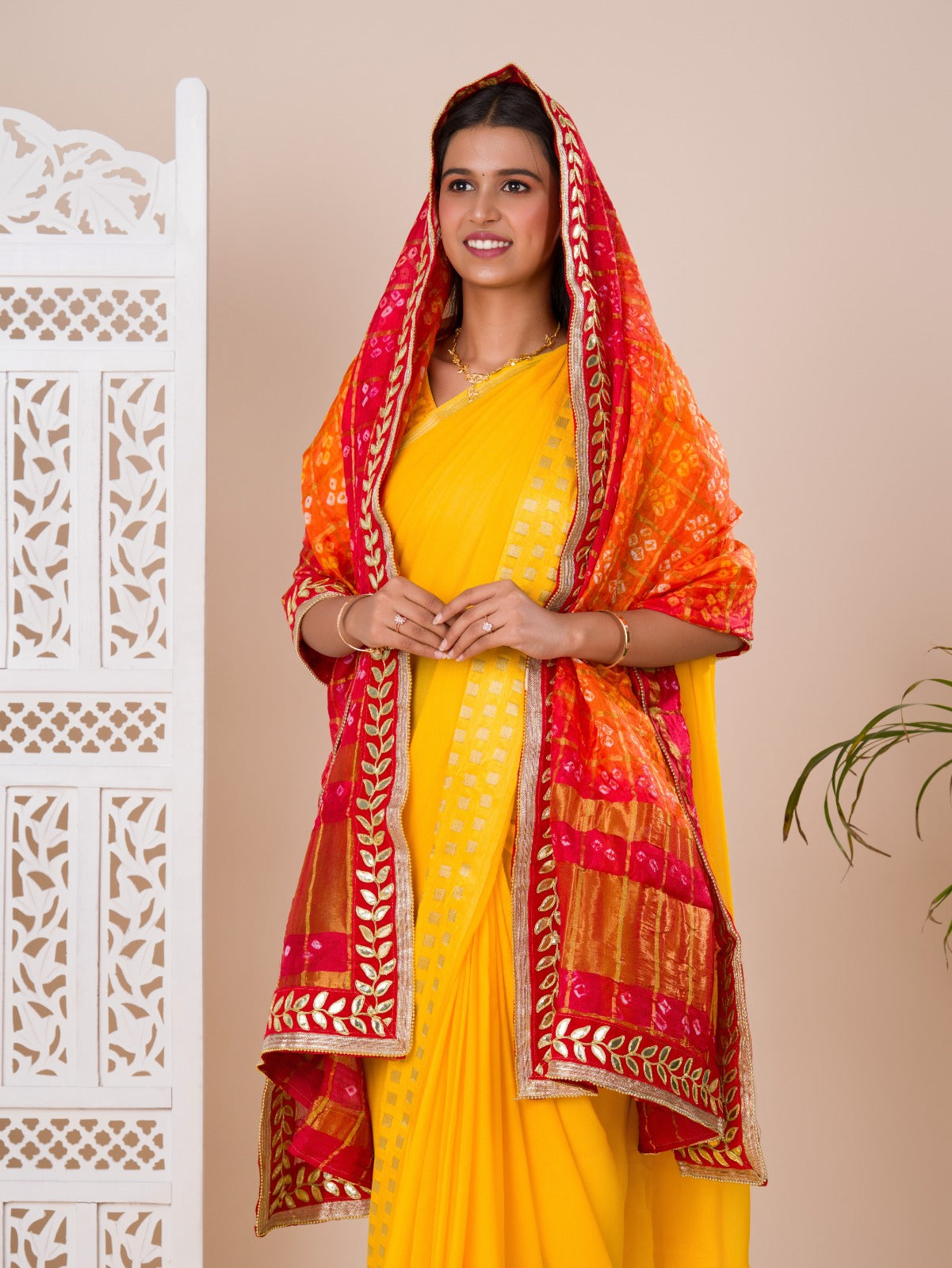 Atraditional Rajasthani Bandhani Chunri dupatta in silk, primarily in red and orange colors with a border, draped over her shoulders.